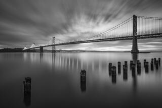 Monochromatic, long exposure sunrise photo of the San Francisco-Oakland bay bridge.