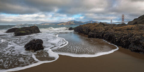 Baker Beach in San Francisco with waves washing around rocky shoreline and Golden Gate Bridge in the background