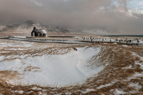 Búðir Black Church in Iceland with snow-covered field, mountains, and coastal landscape