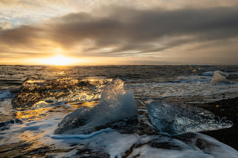 Diamond Beach in Iceland at sunset with glowing ice on the shore and ocean waves in the background
