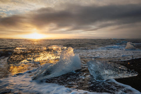 Diamond Beach in Iceland at sunset with glowing ice on the shore and ocean waves in the background