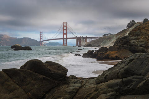 Golden Gate Bridge seen from Marshall's Beach with rocky shoreline and overcast coastal conditions