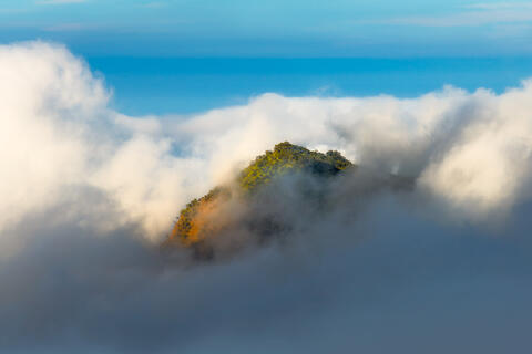 Nā Pali Coast on Kauai with steep green cliffs rising through low clouds above the Pacific Ocean