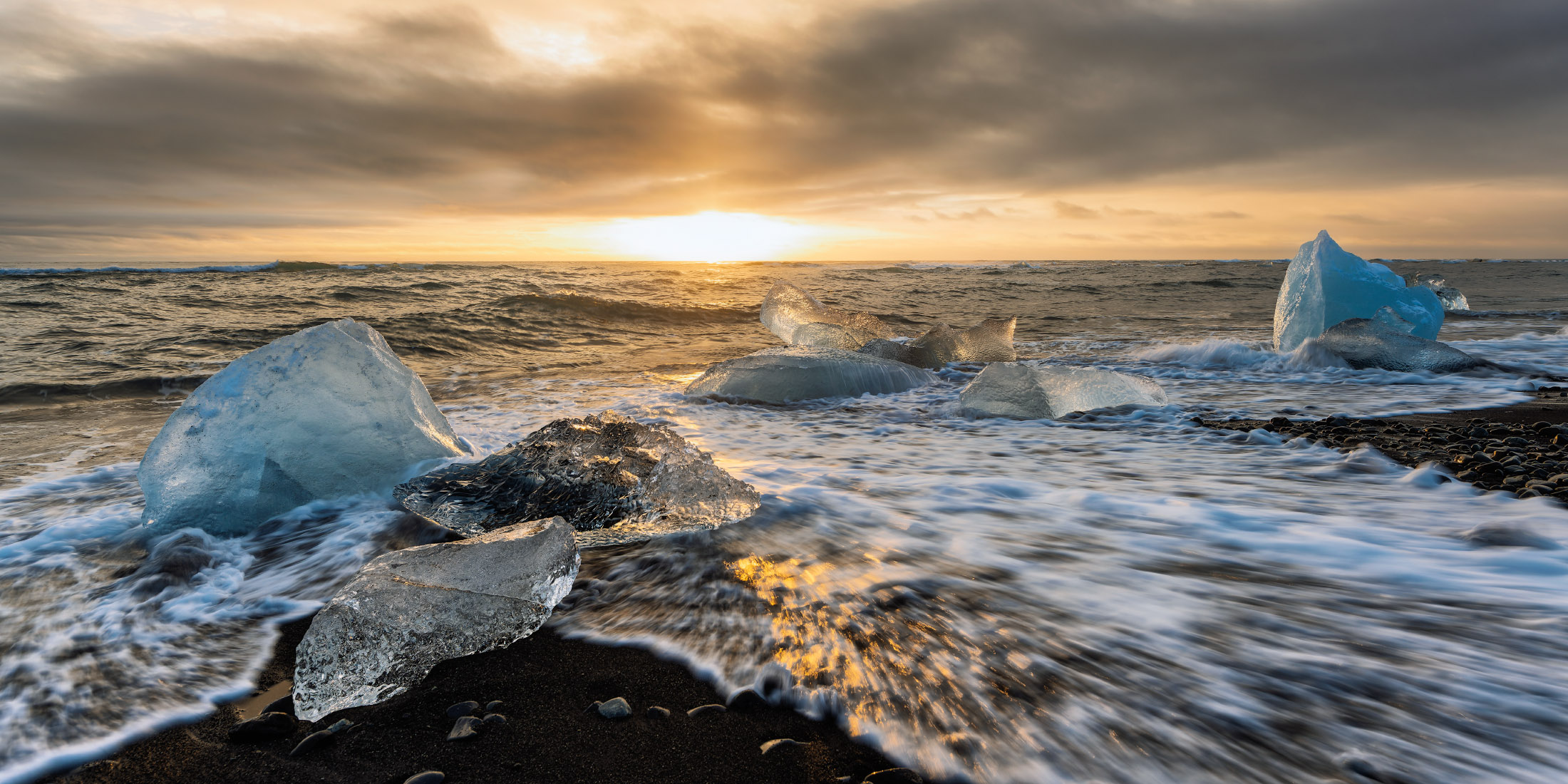 Various ice chunks line the shore of Diamond Beach in Iceland at sunset.