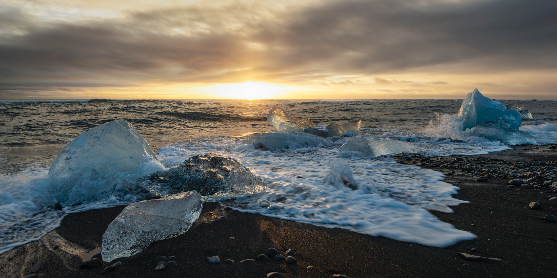 Magic Hour Diamond Beach in Iceland at sunset with ice fragments along the shoreline and waves breaking on black sand