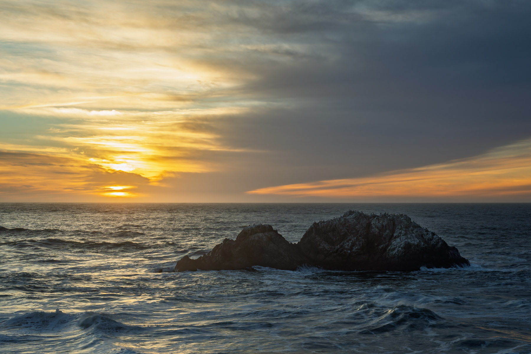 Sundowner Party Lands End in San Francisco with a single sea stack and sunset light over the Pacific Ocean