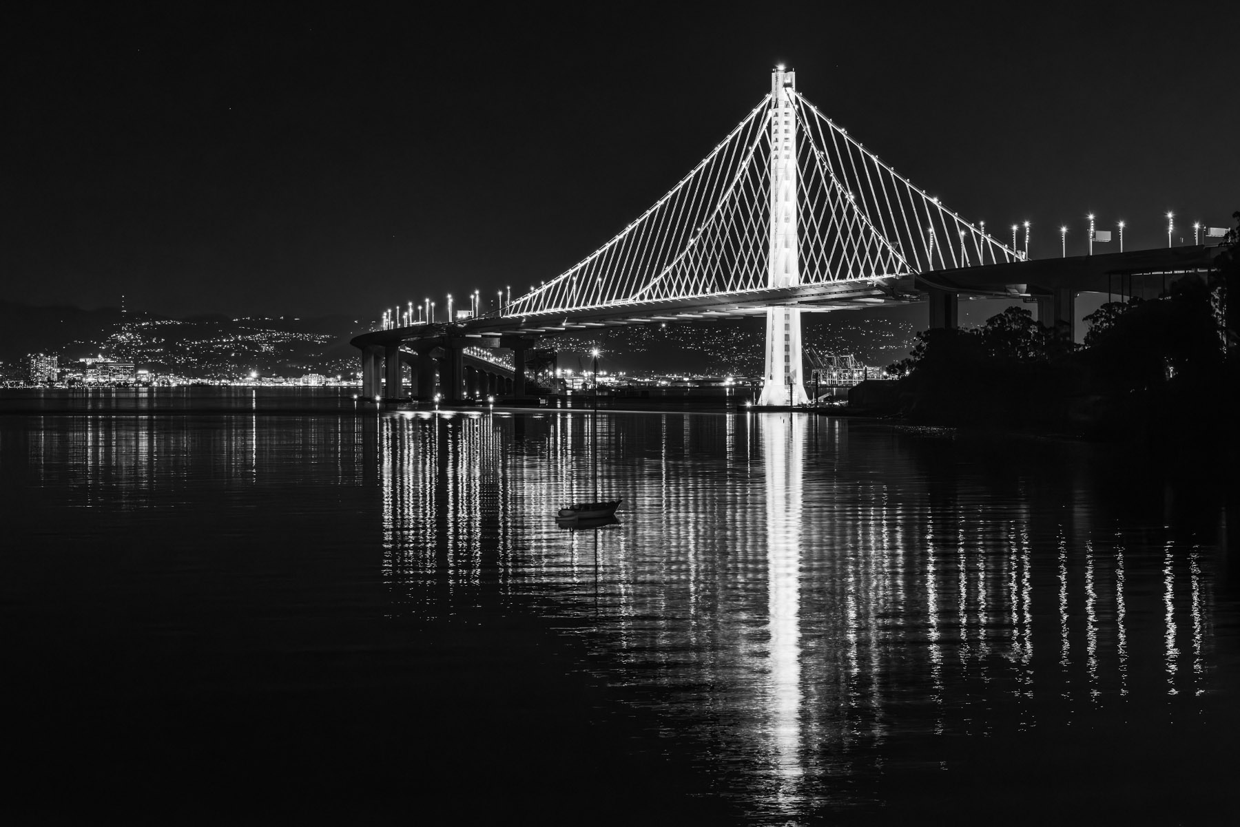 The east span of the San Francisco/Oakland bay bridge casts bright light on a small boat.